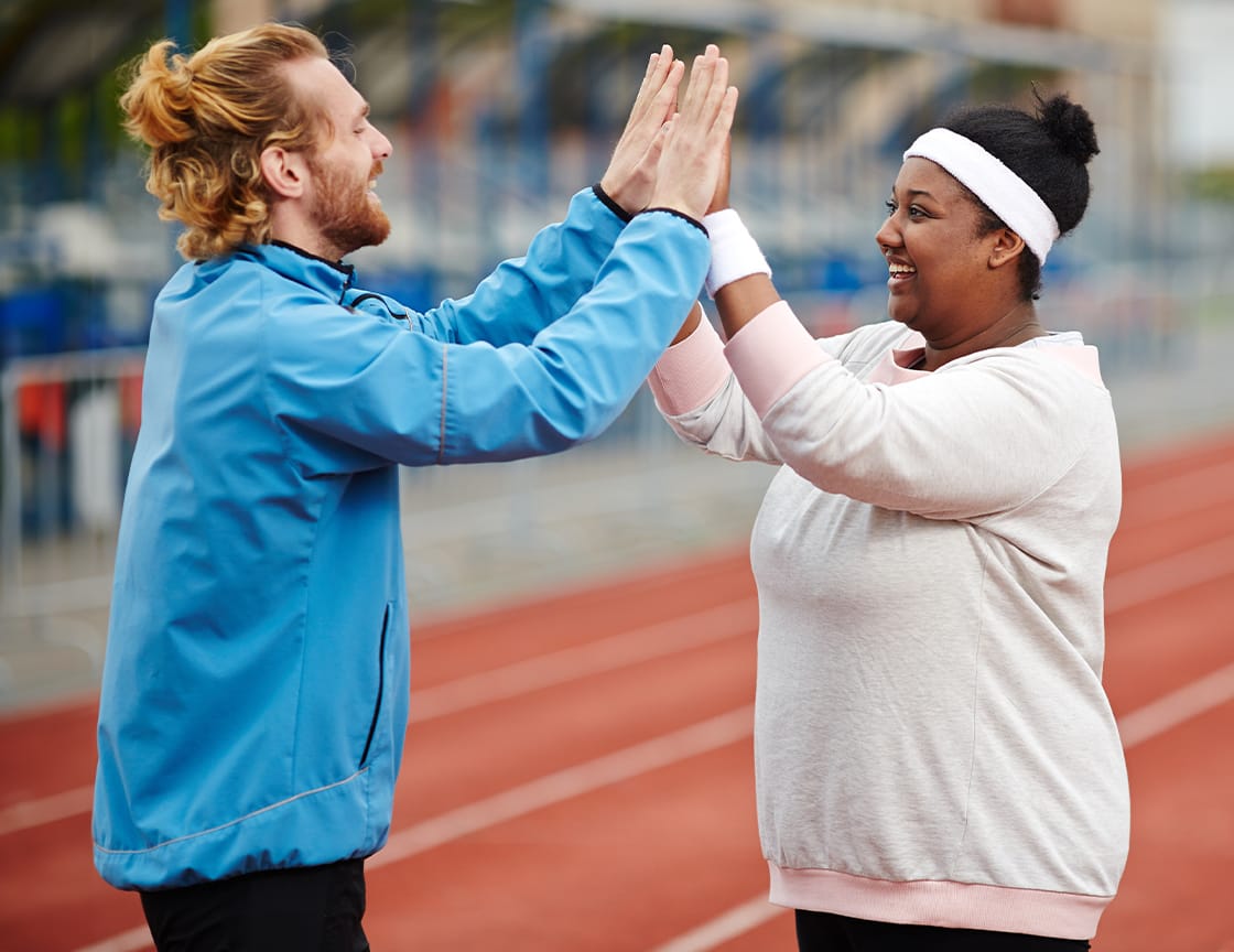 Two friends, a man and a woman, smiling and congratulating each other after a workout or run. They appear happy and supportive of one another.